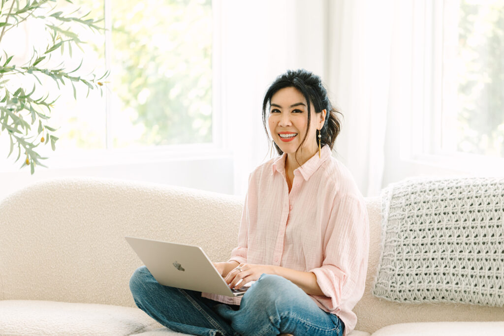 Female entrepreneur working on her laptop in a cozy, light-filled room during a professional brand photoshoot.