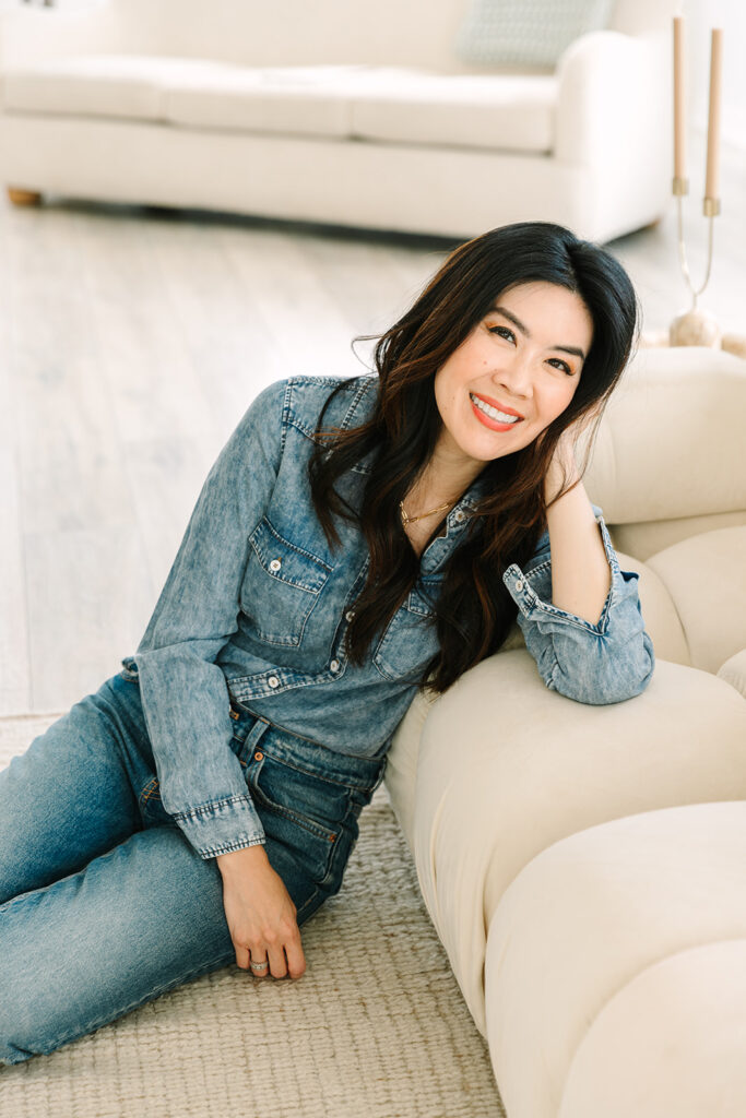 Female entrepreneur smiling while leaning on a couch in a bright living room during a professional brand photoshoot.