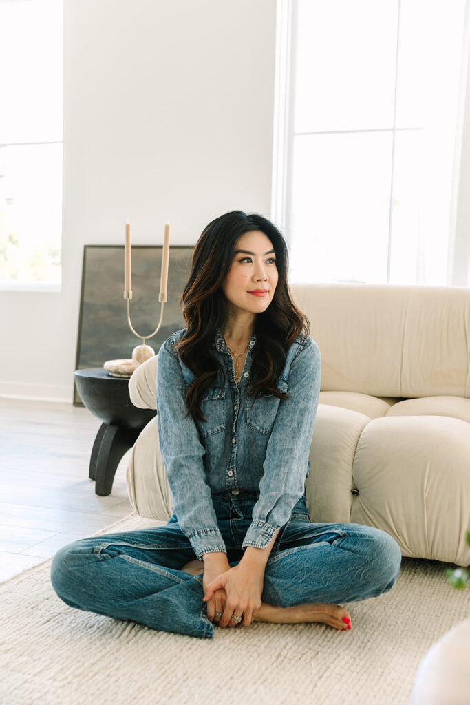 Female entrepreneur seated cross-legged in a denim outfit in a bright, modern living room.