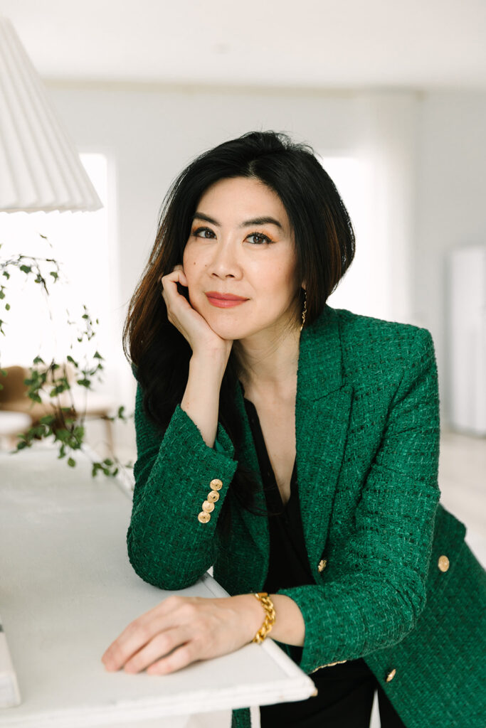 Portrait of a beauty brand founder leaning against a table, wearing a stylish green blazer.