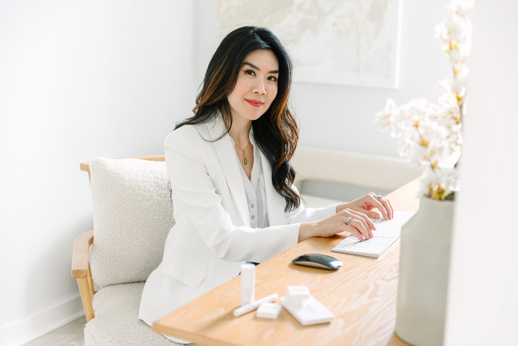 Female entrepreneur typing on a keyboard at her desk during a brand photoshoot, surrounded by beauty products.