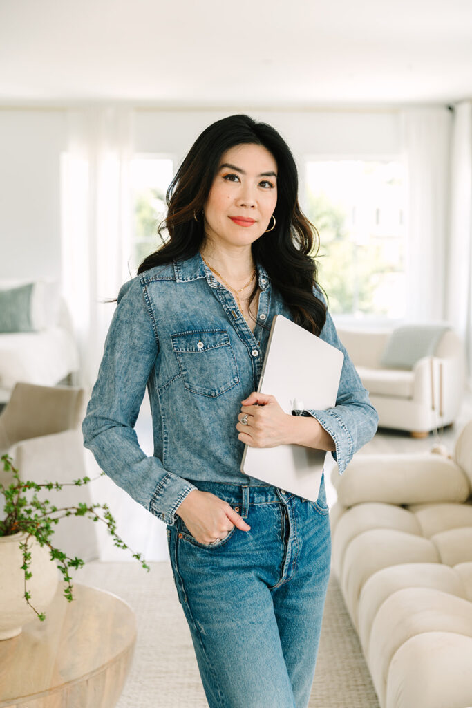 Female entrepreneur standing confidently in denim attire, holding a laptop during a professional brand photoshoot.